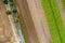 Abstract vertical aerial view of a narrow country road at the edge of an area of arable land with different coloured stripes