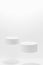 Abstract white scene mockup - two round white cylinder podiums, soar in hard light, shadow.