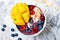 Acai breakfast superfoods smoothie bowl with mango, blueberry, cherry, coconut flakes. Overhead, top view