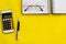 Accounting, financial concept, flat lay or top view of pen, smart phone with calculator with white notepad on vivid yellow backgro