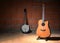 Acoustic guitar and a blurry banjo the background  against a raw brick wall in the rehearsal room of a garage band, copy space,