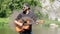 Acoustic guitar emits black smoke. Bearded Caucasian guy in a shirt, cap and sunglasses funny pretends to be playing music. A stra