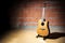 Acoustic guitar in front of a raw brick wall in the rehearsal studio of a garage band, copy space