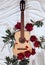 An acoustic wooden guitar lies on a white sheet surrounded by red peonies