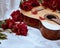 An acoustic wooden guitar lies on a white sheet surrounded by red peonies