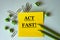 ACT FAST! - word on a yellow note paper on a light background with pencils, crumpled pieces of paper and paper clips