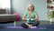 Active aged woman practicing yoga in lotus pose, meditation at home, harmony