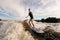 active armless man is surfing on surfboard trails behind boat. Wakesurfing on the river