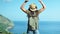 Active backpacker woman traveler in hat and sunglasses enjoying amazing seascape raising hands