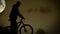 Active biker runs with bicycle in night moonlight