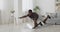 Active black man standing on all fours and practicing swinging legs exercise at home, raising hand and leg