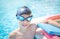 Active child (boy) in cap, sport goggles ready to learns professional swimming with pool board and swim noodles.