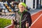 Active elderly Caucasian elderly women of 90 years practice Nordic walking with ski poles on a track with a red rubber coating.