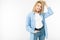 Active emotional blonde girl in jeans and a blue shirt standing against a white wall with copy space