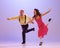 Active and emotional couple in colorful retro style costumes dancing incendiary dances  on purple background in