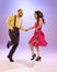 Active and emotional couple in colorful retro style costumes dancing incendiary dances  on purple background in