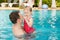 Active father teaching his toddler daughter to swim in pool on tropical resort .