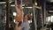 Active fit girl making pullups in fitness center. Trainer helping client at gym