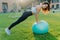 Active fitness woman does gymnastic outdoor with inflated fit ball, has active workout, makes physical exercises in open air,