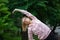 Active fitness woman in pink clothes and eyeglasses is stretching outdoor in the park during spring or summer morning