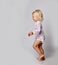 Active frolic blonde kid baby girl in jumpsuit one-piece with floral print pattern runs passes by camera. Side view.