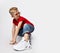 Active, frolic blonde kid boy in red t-shirt, blue jeans, white sneakers and sunglasses is in ready to run position