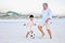 Active grandfather and grandson playing soccer on sandy beach. Cute little boy kicking ball with his grandpa