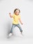 Active happy screaming kid baby girl blonde in yellow t-shirt, blue jeans and sneakers is jumping high, having fun