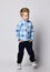 Active happy smiling blond kid boy in blue pants, fleece jacket sweater with stars print pattern and white sneakers