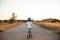 Active healthy sport small kid in helmet and blue denim shorts standing on empty asphalt way with scooter on summer sunset leisure