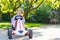 Active little boy driving pedal car in summer garden
