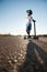 Active little boy in helmet and sunglasses standing on asphalt empty highway with scooter in summer heat desert