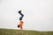 Active little caucasian boy in jeans standing on hands upside down on green grass outdoors with copy space