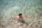 Active little caucasian kid in goggles diving in sea clear water with stony bottom during summer travel leisure vacation