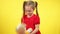 Active little girl shaking doll at yellow background. Portrait of hyperactive Caucasian child playing with toy