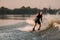 active man holds cable and energetically rides down on splashing wave on wakeboard.