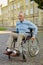 Active mature recovering man in wheelchair smiling away while spending time alone in the park near hospital