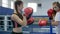 Active people, girl takes blows on boxing paws of strong female athlete on ring in gym