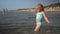 Active playful little girl dance wading through sea water waves. Funny child