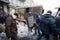 Active protester with shield and mask stands near the burned military auto on the winter street during anti-government riot