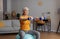 Active retirement. Happy senior woman in sportswear exercising with dumbbells on fitball, having domestic training