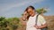 Active senior Asian woman with backpack smiles, removes sunglasses atop mountain. Mature hiker enjoys sunny hike