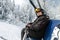 Active senior experienced mature old person in ski helmet, goggles and black suit sit resting on ski lift mountain peak