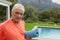 Active senior man standing with exercise mat near poolside in the backyard