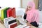 Active smart asian muslim woman in blue suit and pink shaft sitting and holding credit card while using mobile phone for payment