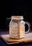 Active sourdough starter in glass jar. Rye leaven for bread on wooden cutting board on black background. Close-up. Dark low key