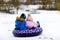 Active toddler girl and school boy sliding together down the hill on snow tube. Children, siblings having fun outdoors