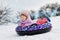 Active toddler girl sliding down the hill on snow tube. Cute little happy child having fun outdoors in winter on sledge