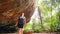 Active woman with backpack explores trail in rocky mountain grotto. Hiker adventure through natural cave landscape