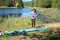 Active woman inflates SUP board with manual pump, beautiful lake and nature on background, stand up paddling